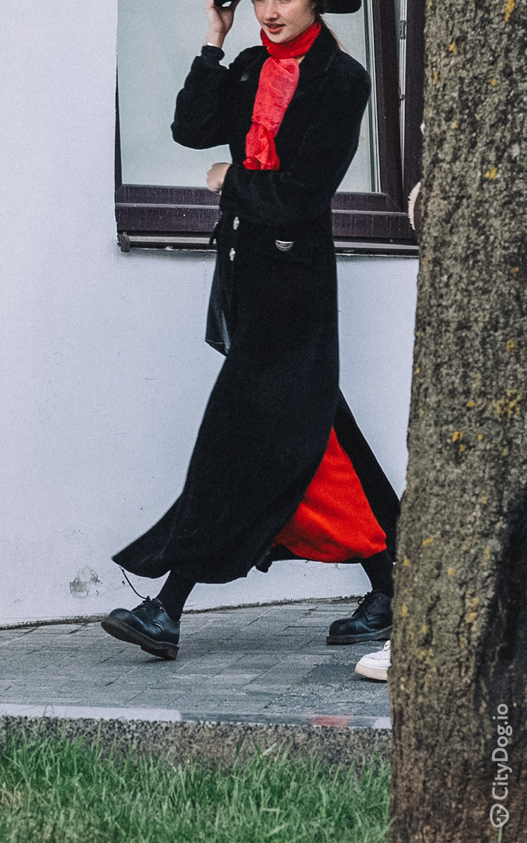 Девушка в длинном черном пальто с красной юбкой.