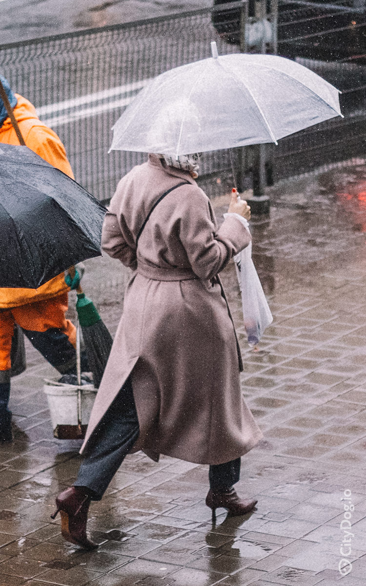 Девушка на высоких каблуках и в пальто идет под зонтом.