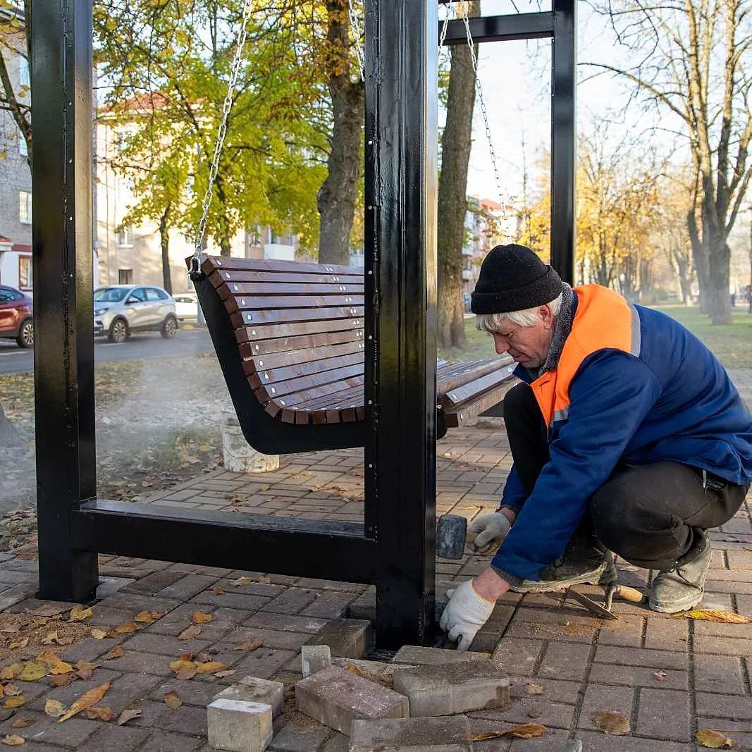 Рабочий устанавливает лавку.