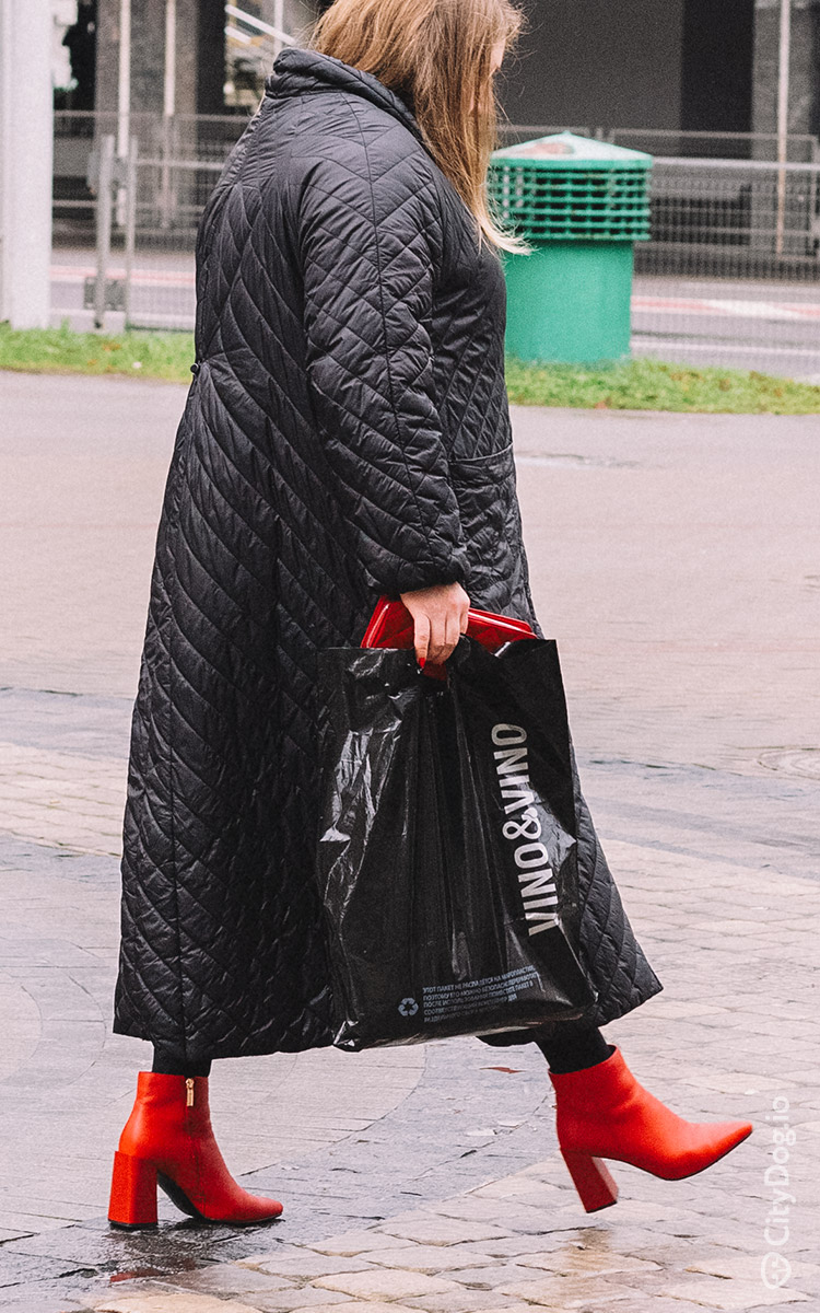 Черное стеганое пальто с красными ботинками и сумочкой.