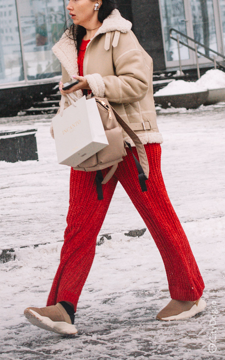 Девушка в бежевой дубленке и красных брюках.