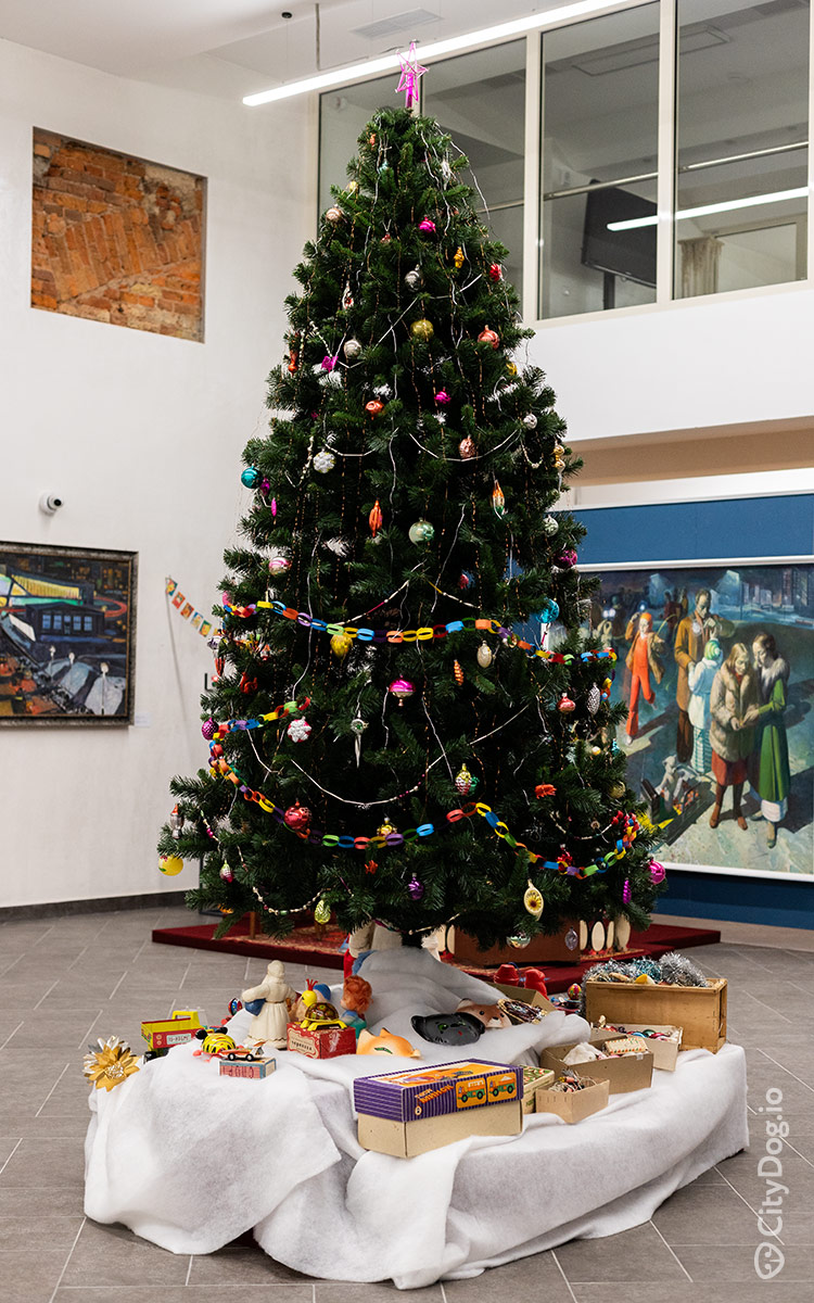 Новогодняя елка, украшенная самодельными гирляндами, на фоне картин.
