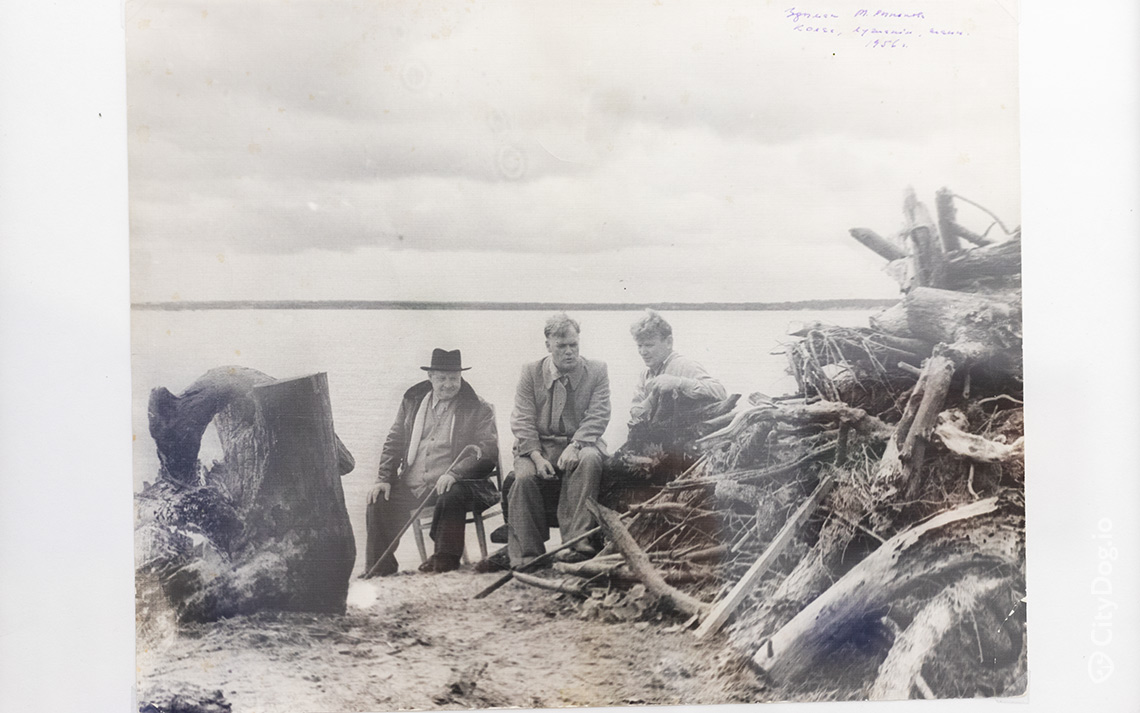 Трое мужчина сидят на берегу озера.