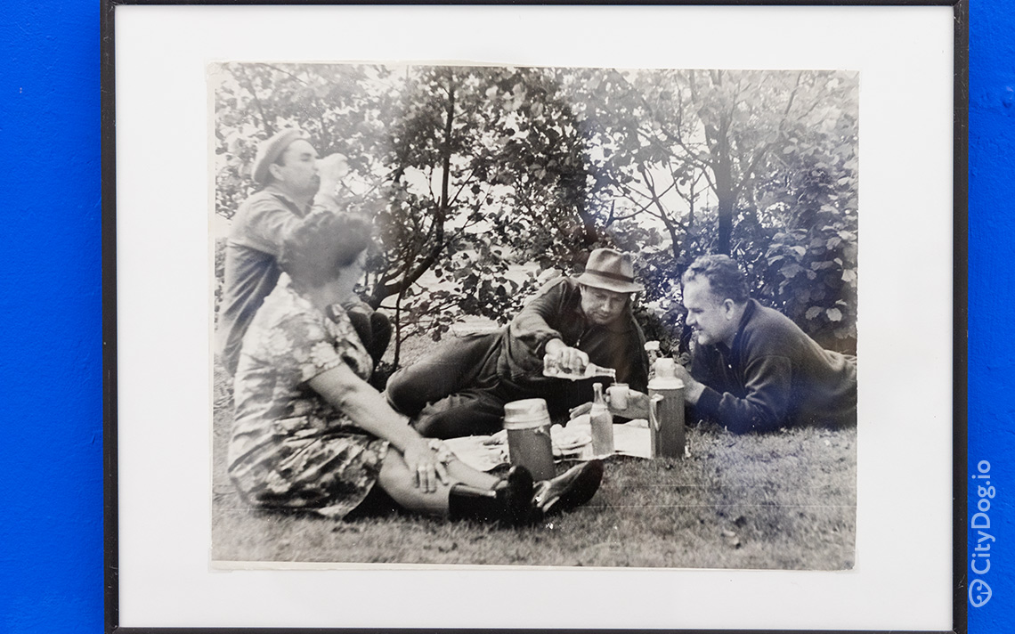 Трое мужчин и женщина обедают на траве в лесу.
