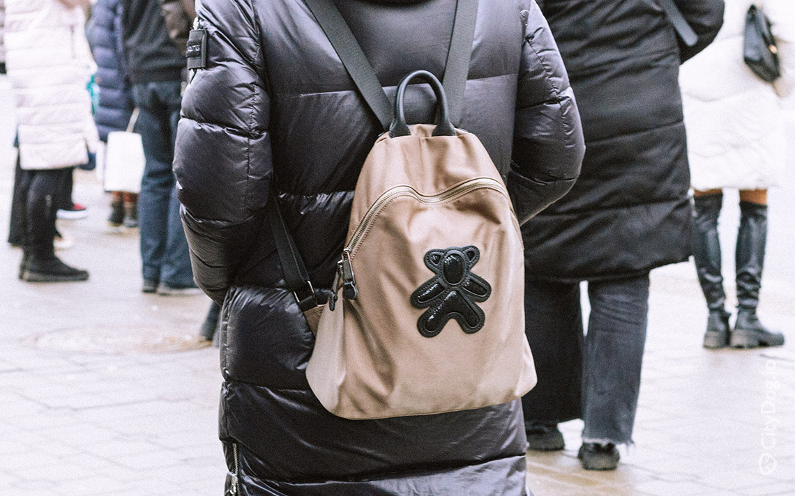 Девушка с коричневым рюкзаком с нашивкой в виде медведя.