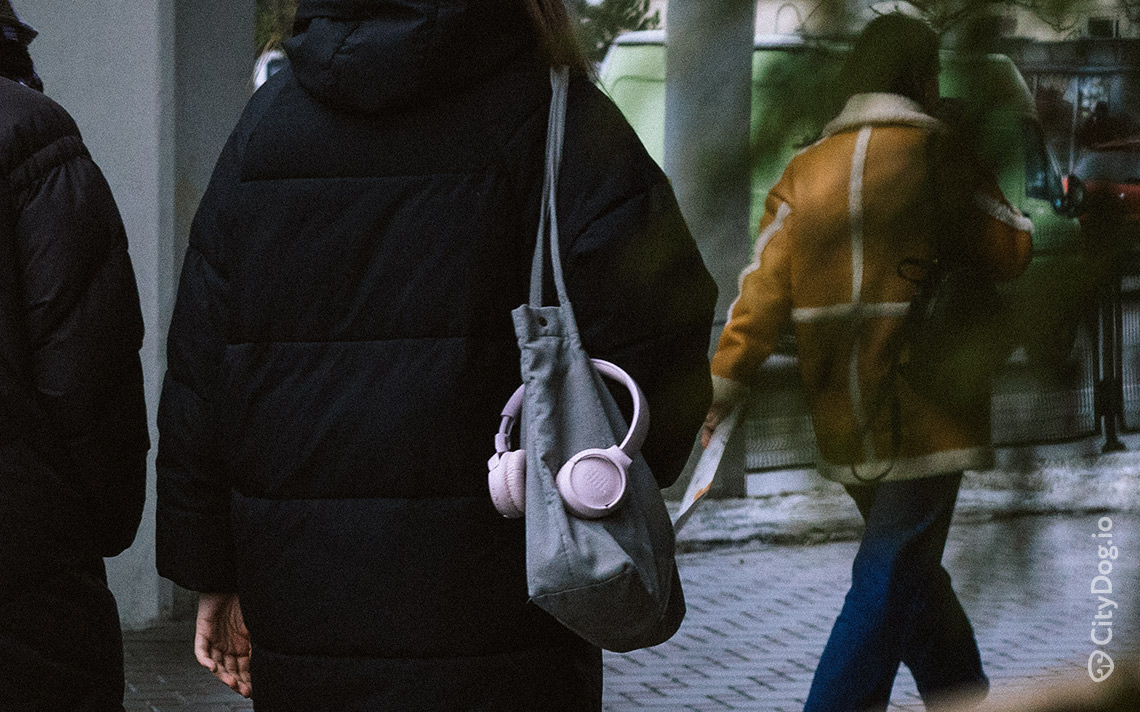 Девушка с серой сумкой на плече и розовыми наушниками.
