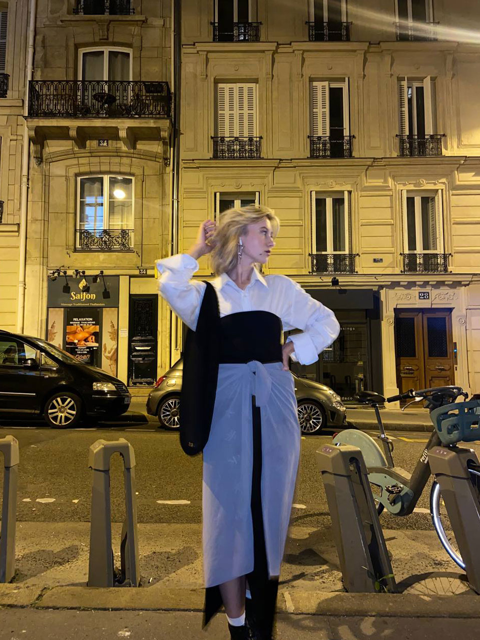 Фото девушки, которая стоит на улице Парижа в белой рубашке, черном корсете и светлым платком, повязанным, как юбка на запах.