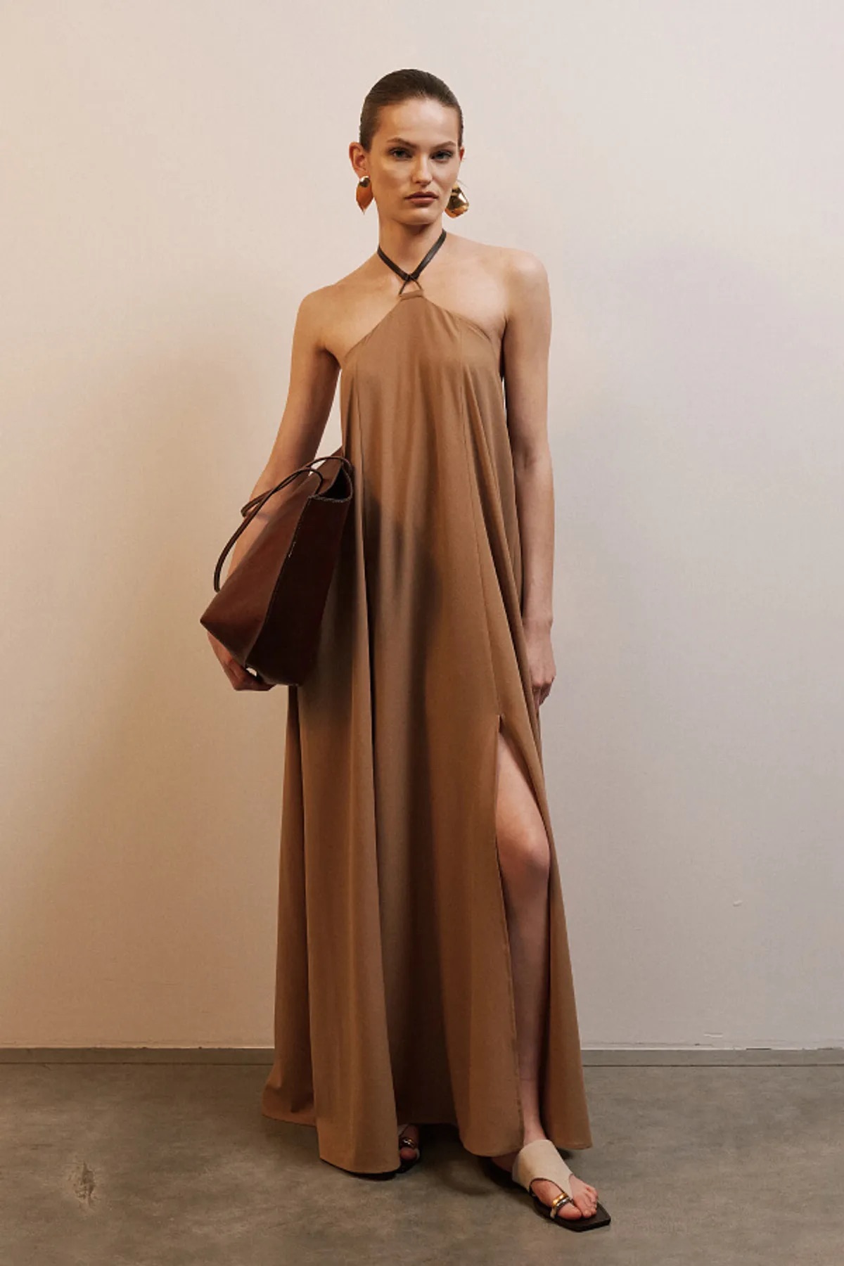 Девушка стоит в длинном, струящемся платье Lsd.clothing с открытой спиной и соблазнительными разрезами.